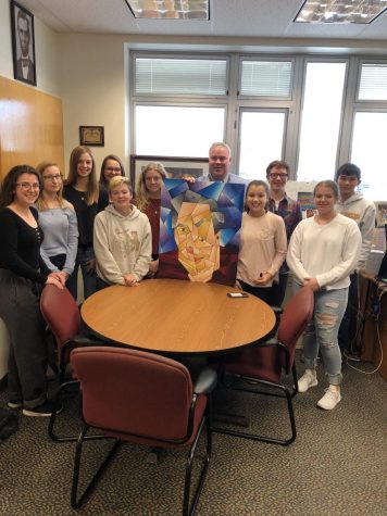Bill August is with the ten freshmen who surprised him with a cubism painting of himself.  After the idea was suggested to the students, they volunteered their time to paint this piece as a surprise for August. 